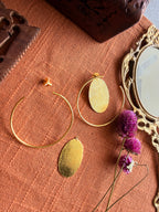 Sama Hoops flatlay showing hoop and detached oval disc separately on terracotta linen, with antique mirror and dried purple flowers