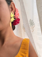 view of woman wearing Apsara danglers with pink and red flowers in hair, mustard embroidered blouse, sheer floral curtain in background