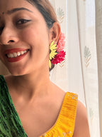 Woman smiling, wearing Apsara danglers styled with flowers in hair, green saree and mustard blouse, soft natural light through sheer curtain