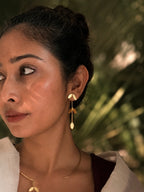 Close-up of woman wearing Pallavi earrings with hair in an updo, gold leaf cascade visible against her neck alongside the Pallavi choker necklace, dark botanical background, warm natural light