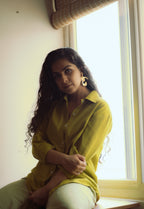 Woman in a light green shirt sitting by a window, wearing Ankur Twist Earrings.