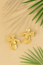 Gold plated floral shaped Ankur Twist Earrings on a beige background with green leaves
