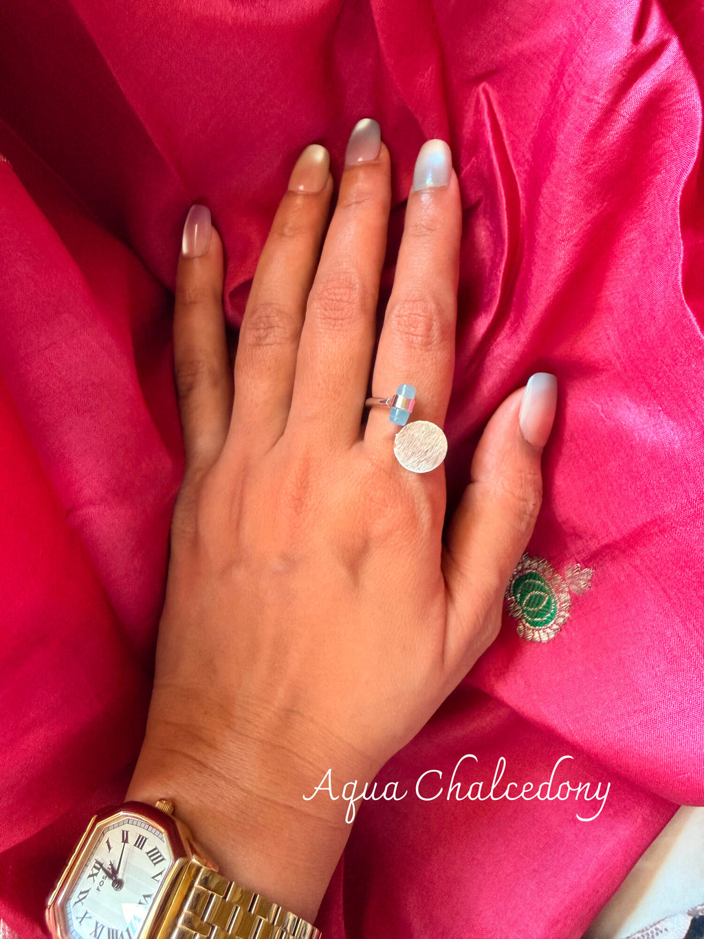 Aqua Chalcedony ring with a pale aqua stone beside a round disc, worn on a hand resting on pink silk
