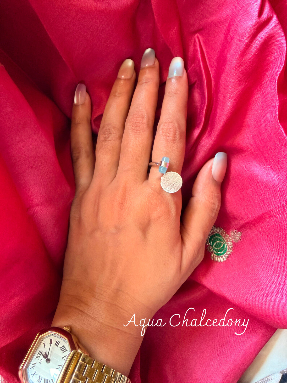 Aqua Chalcedony ring with a pale aqua stone beside a round disc, worn on a hand resting on pink silk