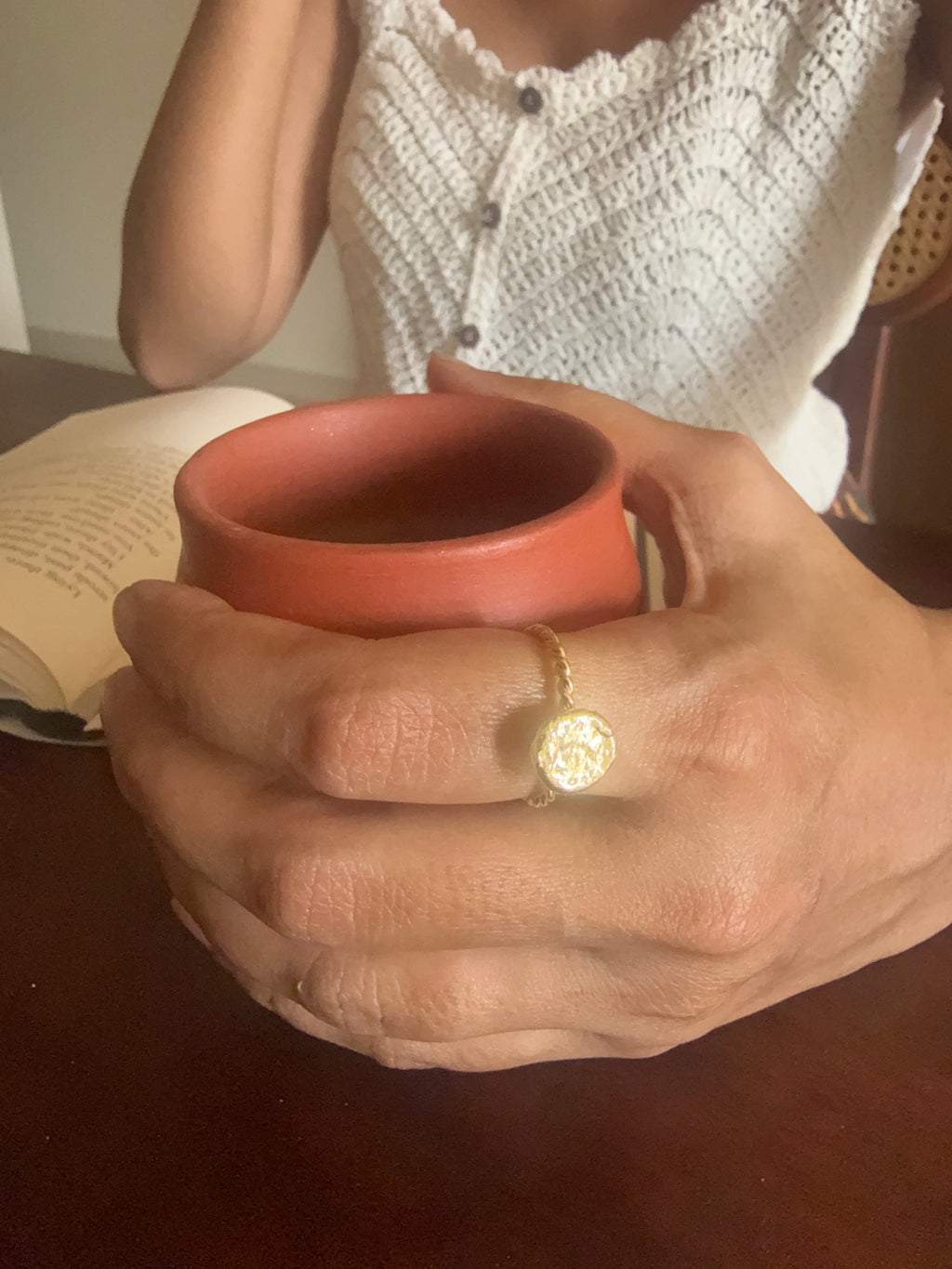 Close-up of woman's hand wearing the Bandhani Ring while holding a terracotta cup, soft natural light