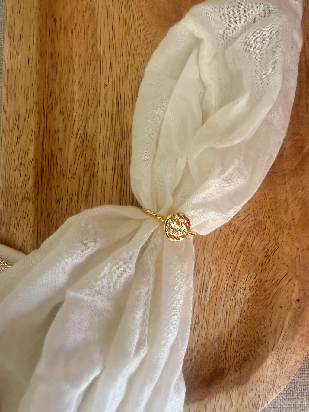 Bandhani Ring resting in a knot of white fabric on a wooden surface, showing the twisted band and textured disc detail