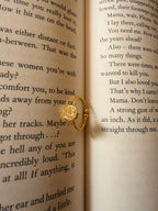 Bandhani Ring placed in the crease of an open book, gold disc catching light against the printed page