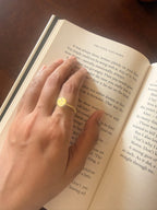 Woman's hand wearing the Bandhani Ring while resting on an open book, warm natural light, relaxed reading moment