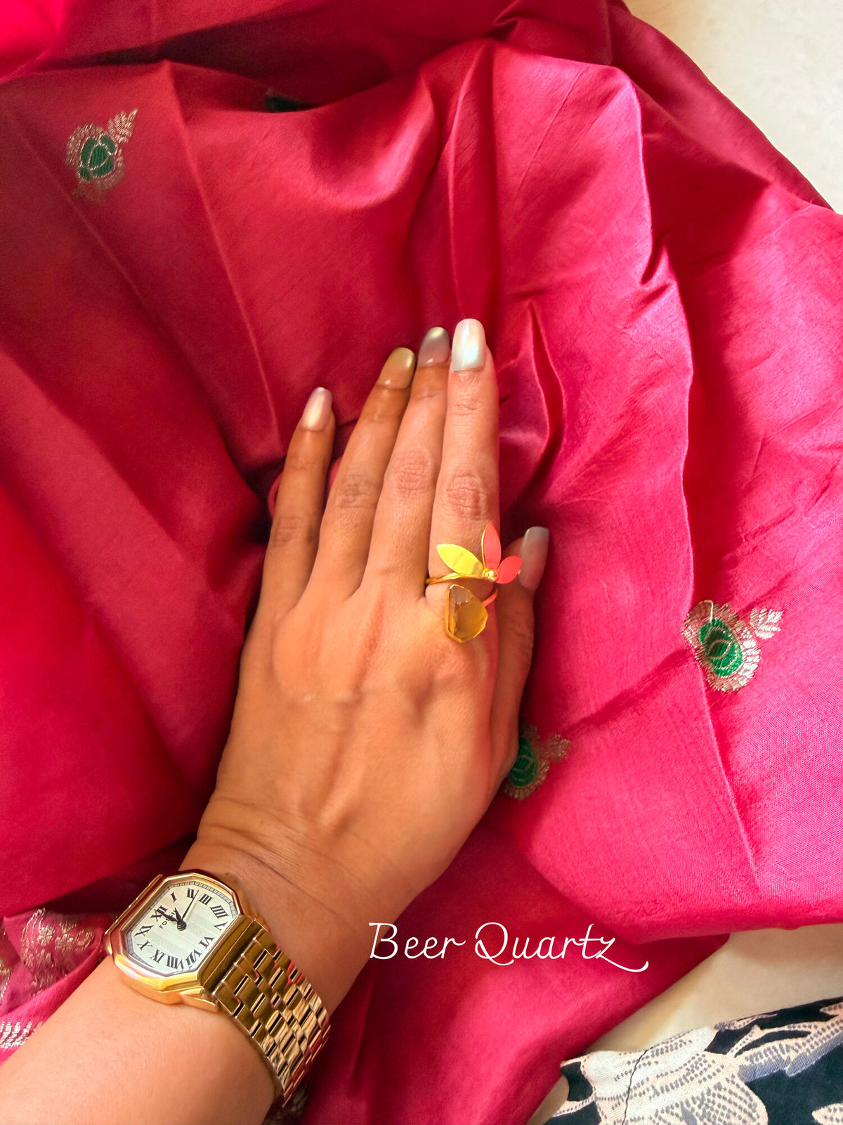 Beer Quartz ring with a raw honey-coloured stone and a gold leaf detail, worn on a hand resting on pink silk