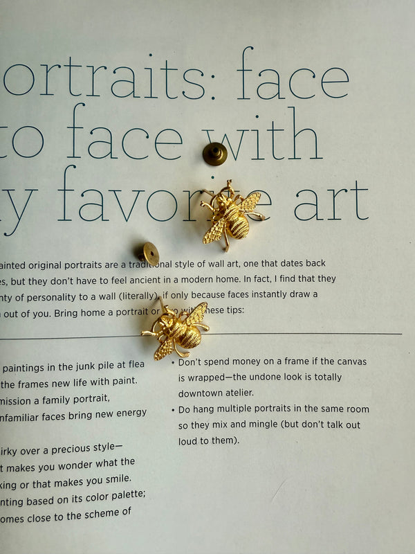 Gold plated honey bee earrings on a magazine page.