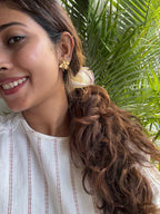 Woman with styled hair and earrings against a green leafy background