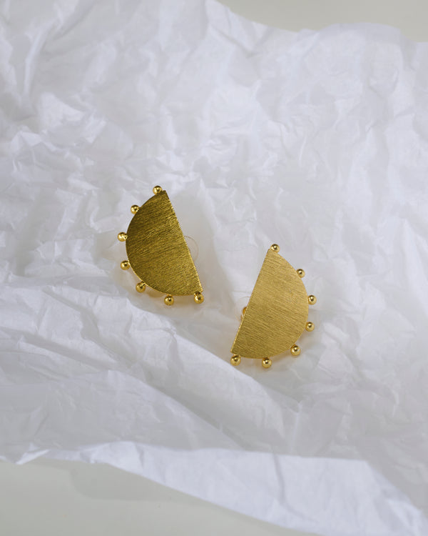 Gold toned half circular earrings with tiny circular details on a white textured paper background.