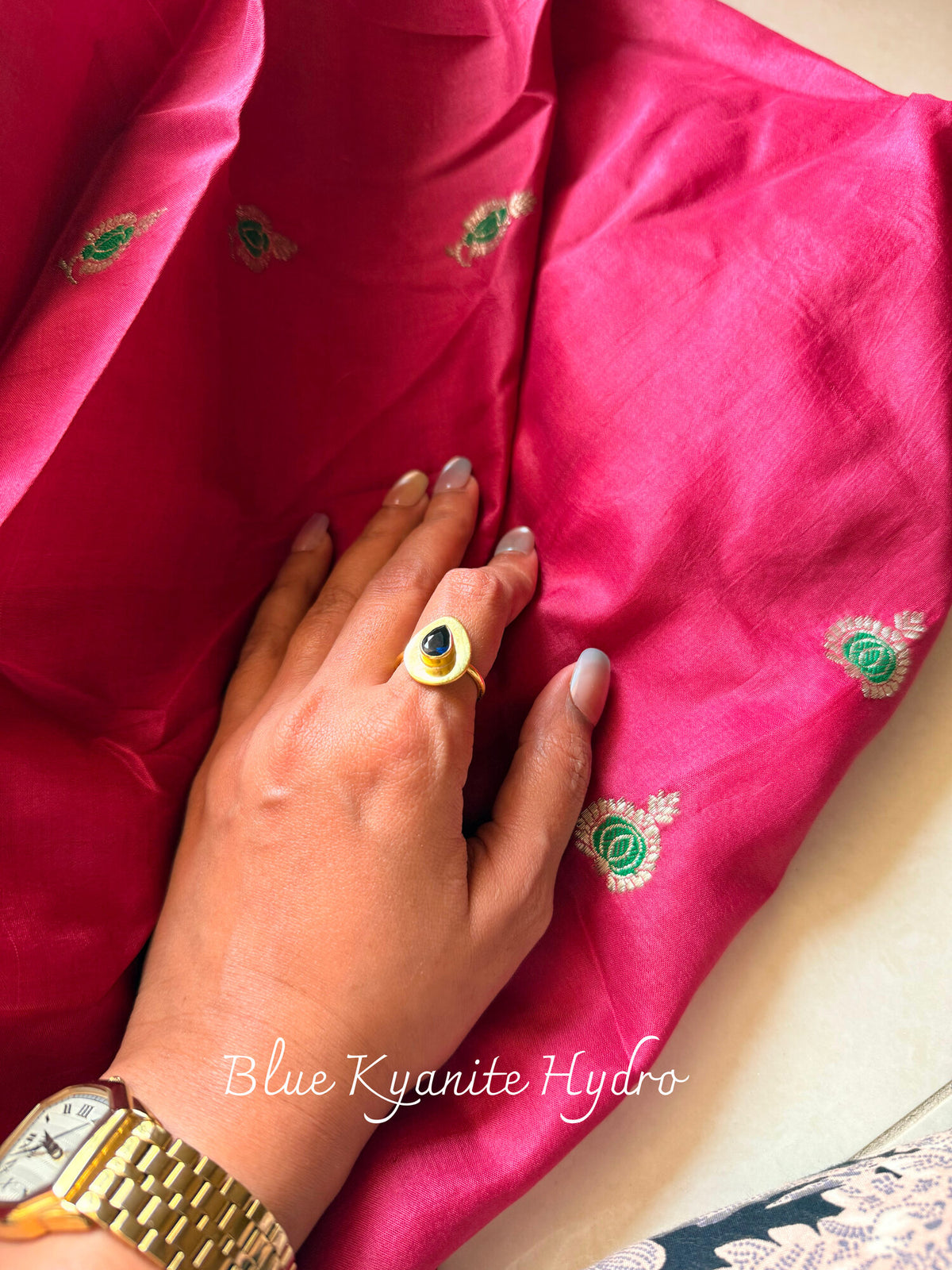 Blue Kyanite Hydro ring with a deep blue stone in a teardrop-shaped matte gold setting, worn on a hand resting on pink silk
