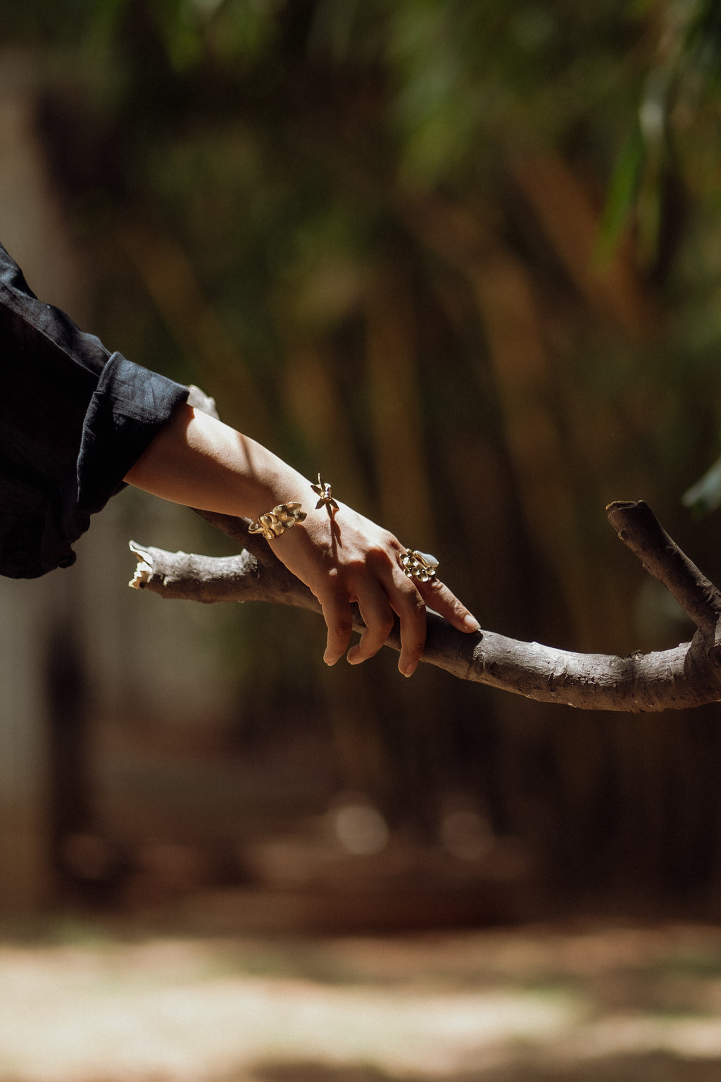 A hand wearing the floral cuff bracelet, hand is resting on a tree branch, blurry green background.