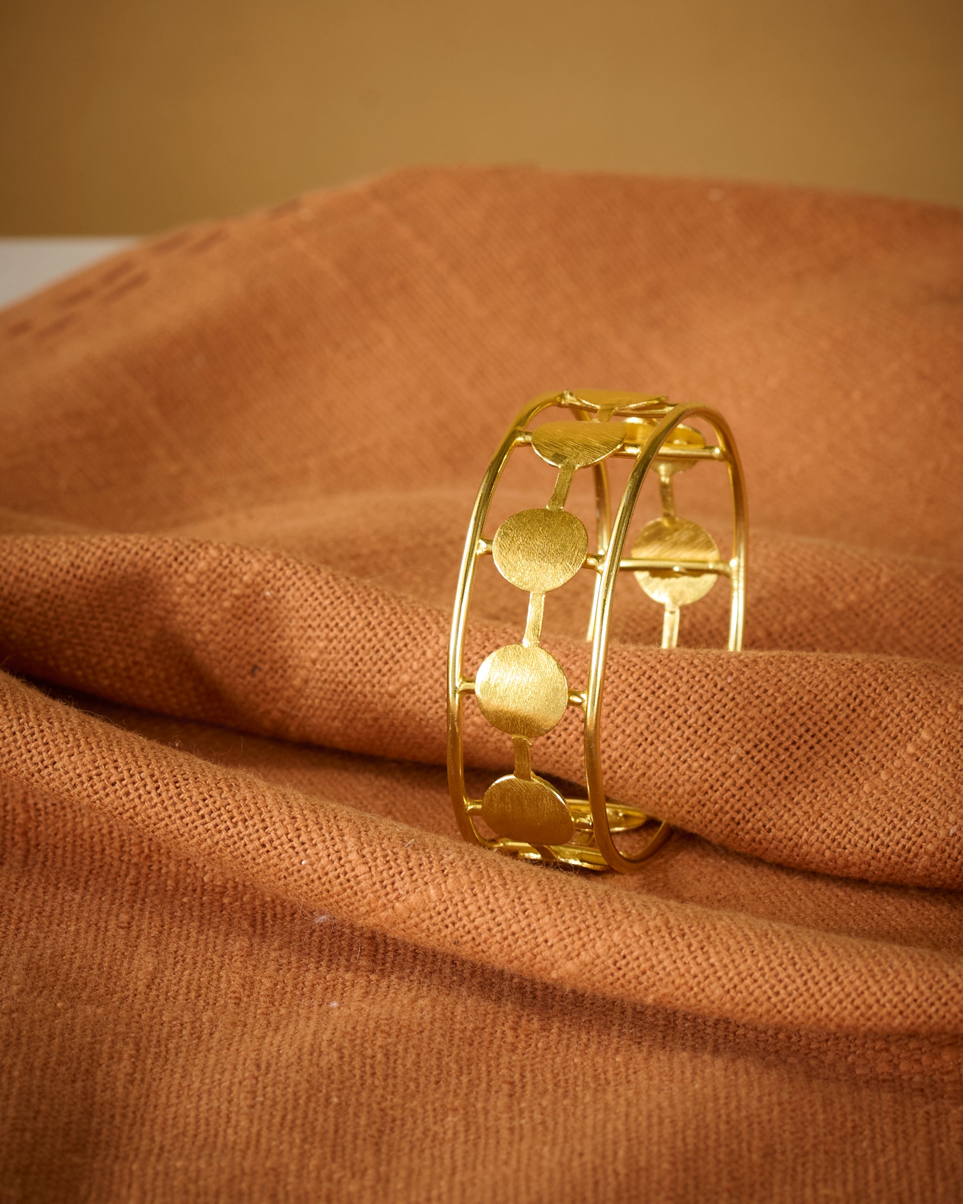 Gold plated circular design bracelet on a brown fabric background