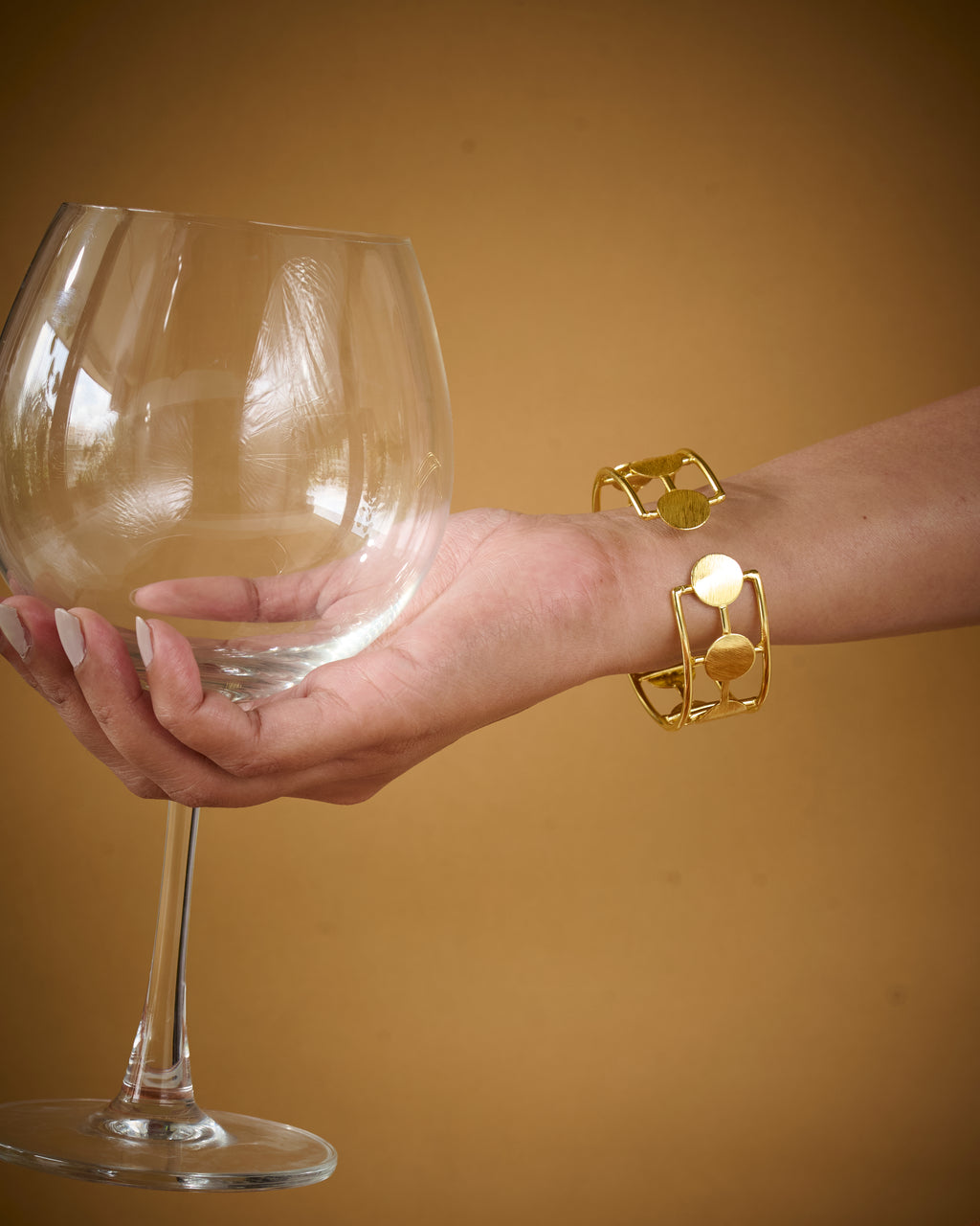 Hand holding a wine glass with a gold bracelet on a yellow background