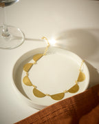 Gold colored necklace with semi-circular pendants on a white dish