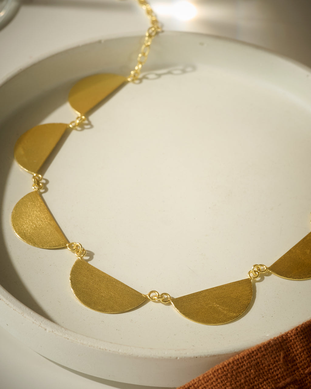 Close up of Gold colored necklace with semi-circular pendants on a white dish