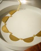 Close up of Gold colored necklace with semi-circular pendants on a white dish