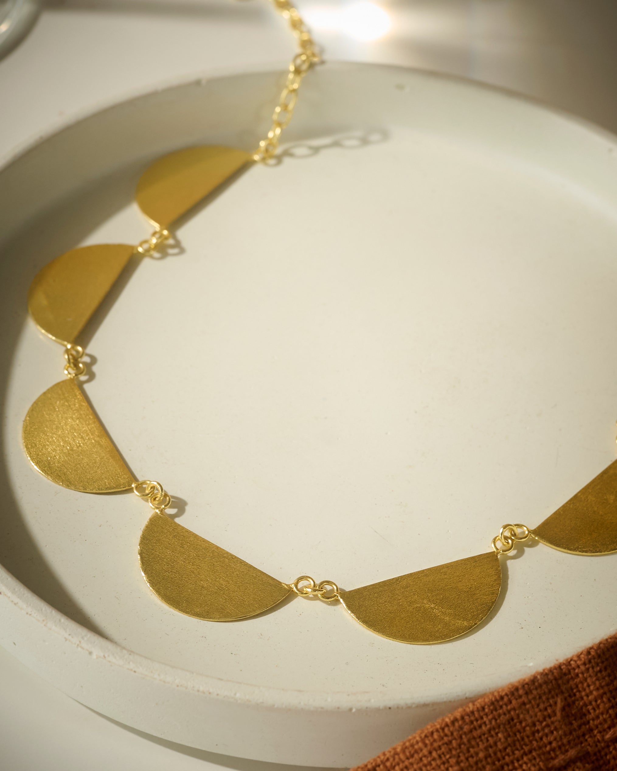 Close up of Gold colored necklace with semi-circular pendants on a white dish
