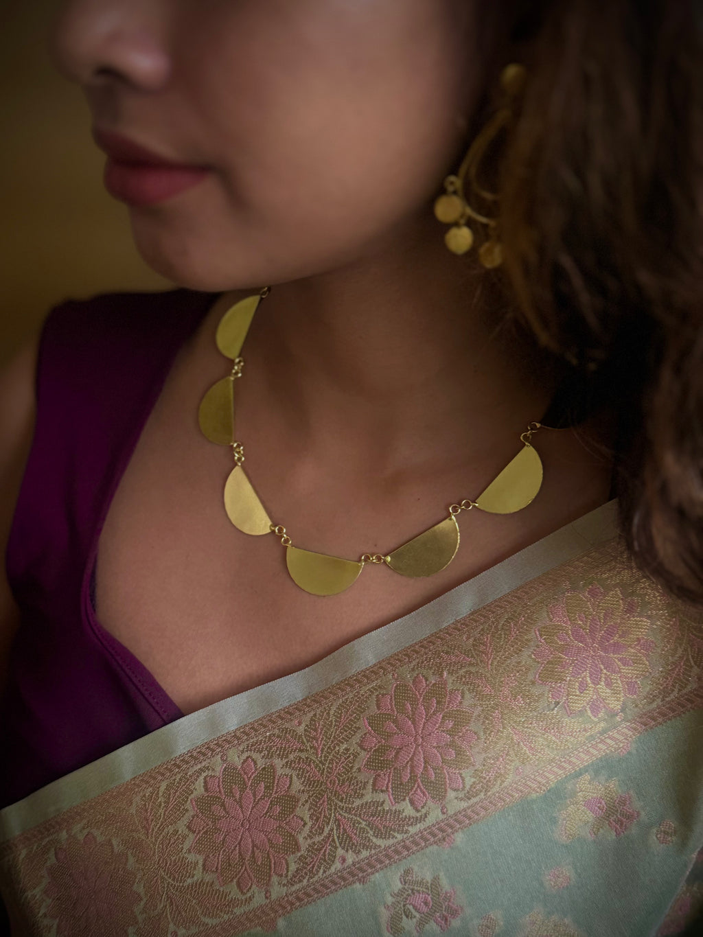 Woman wearing a gold colored necklace and earrings with a floral saree