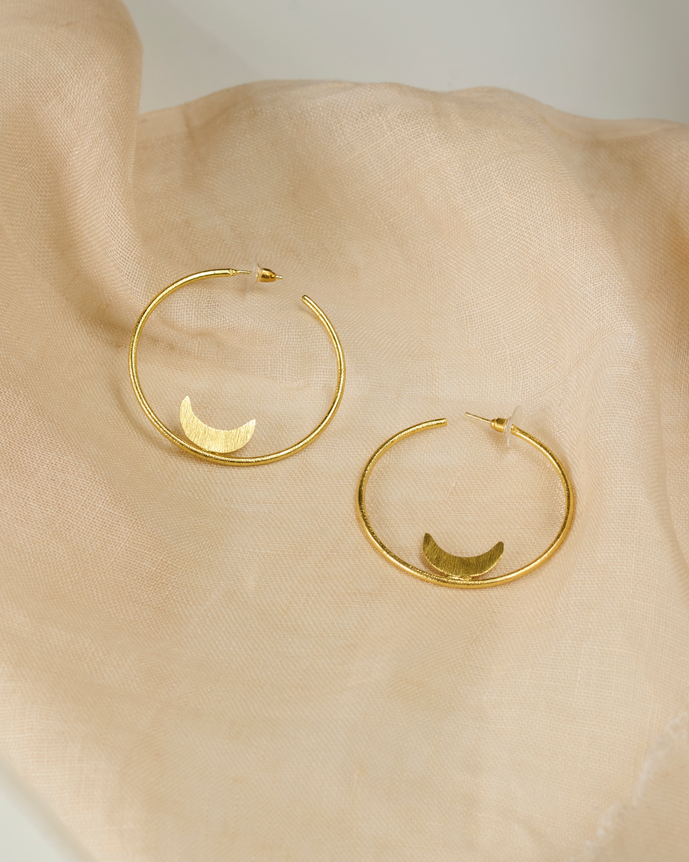 Gold plated hoop earrings with moon detail kept on a neutral color fabric.