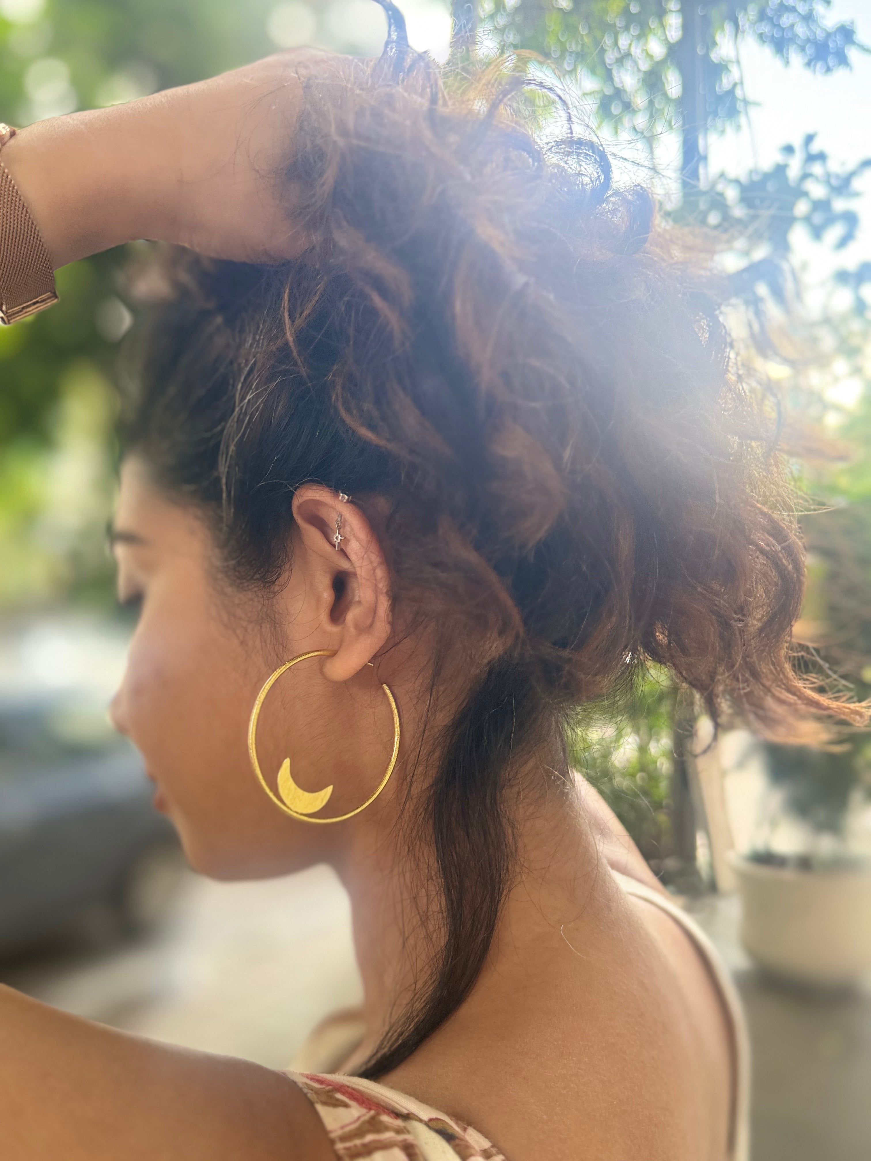 Woman with styled hair and gold hoop earrings outdoors