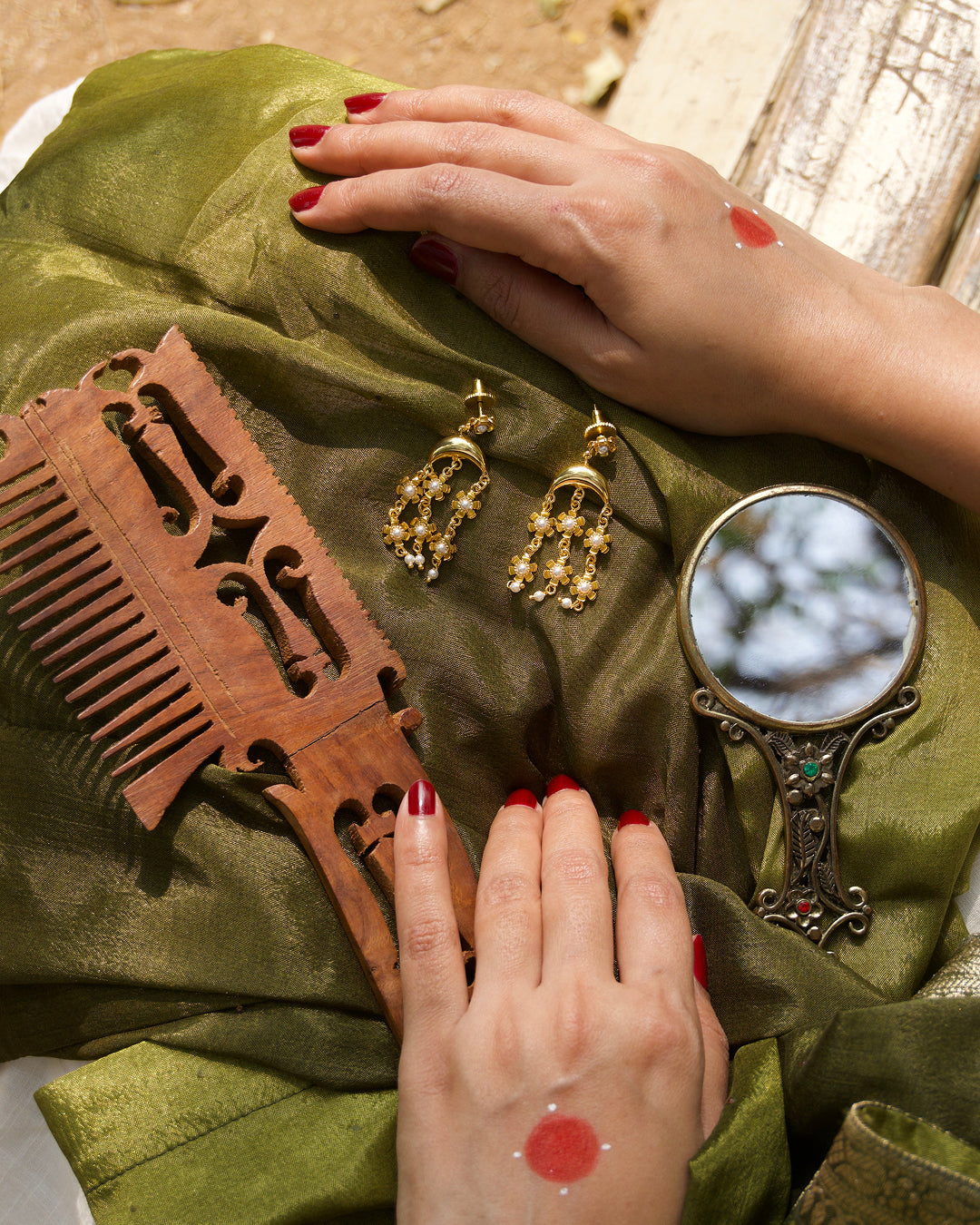 Chandrika danglers kept  with vintage comb and mirror on a green fabric with hands touching the fabric.