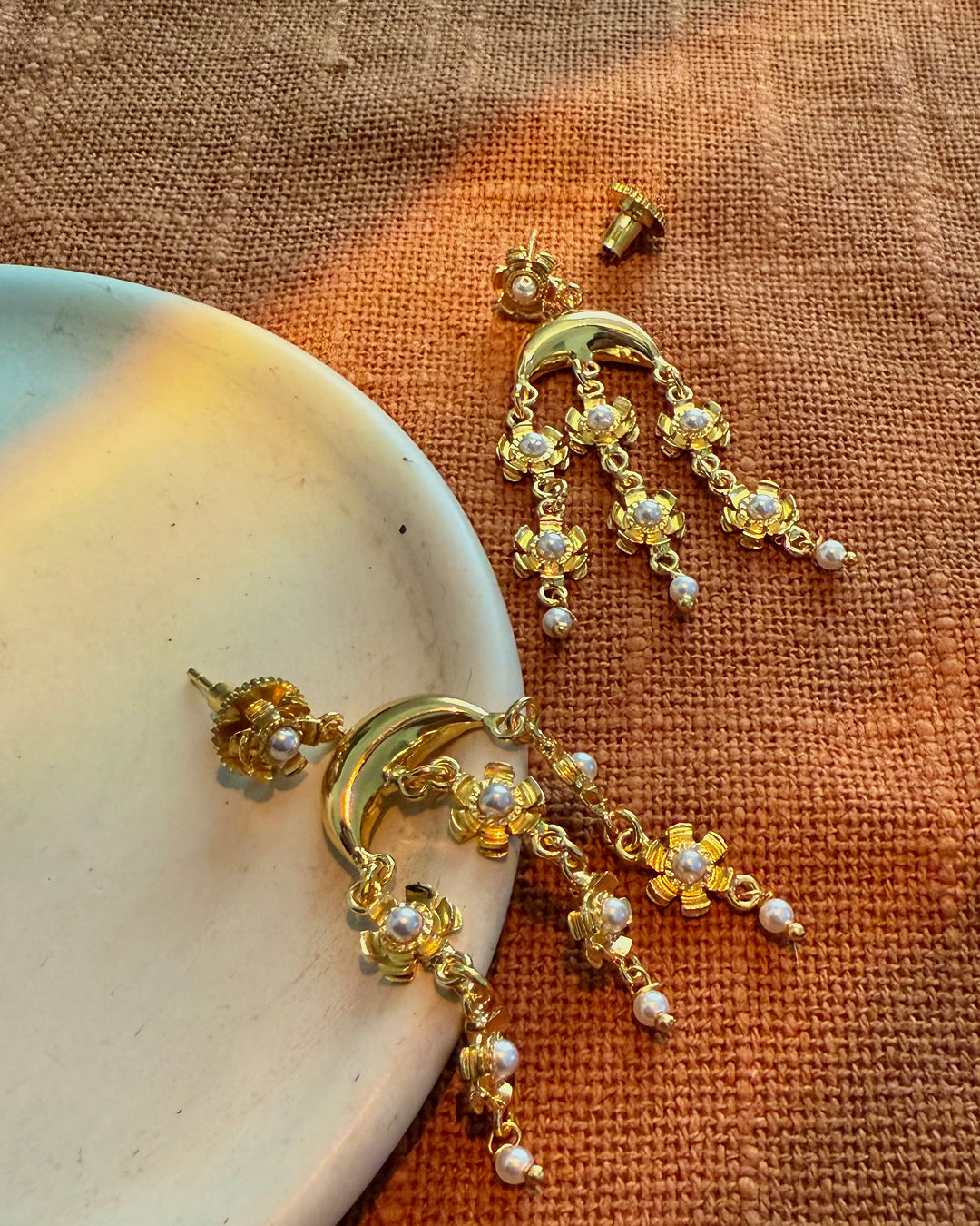 Gold earrings with pearl accents on a textured surface