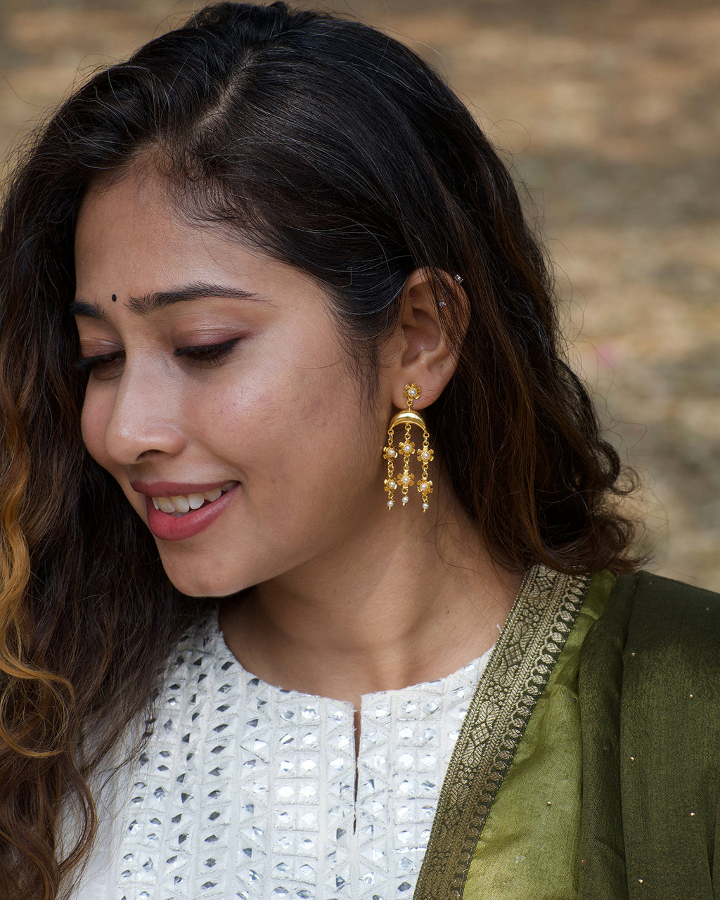 Woman wearing gold earrings with a blurred natural background