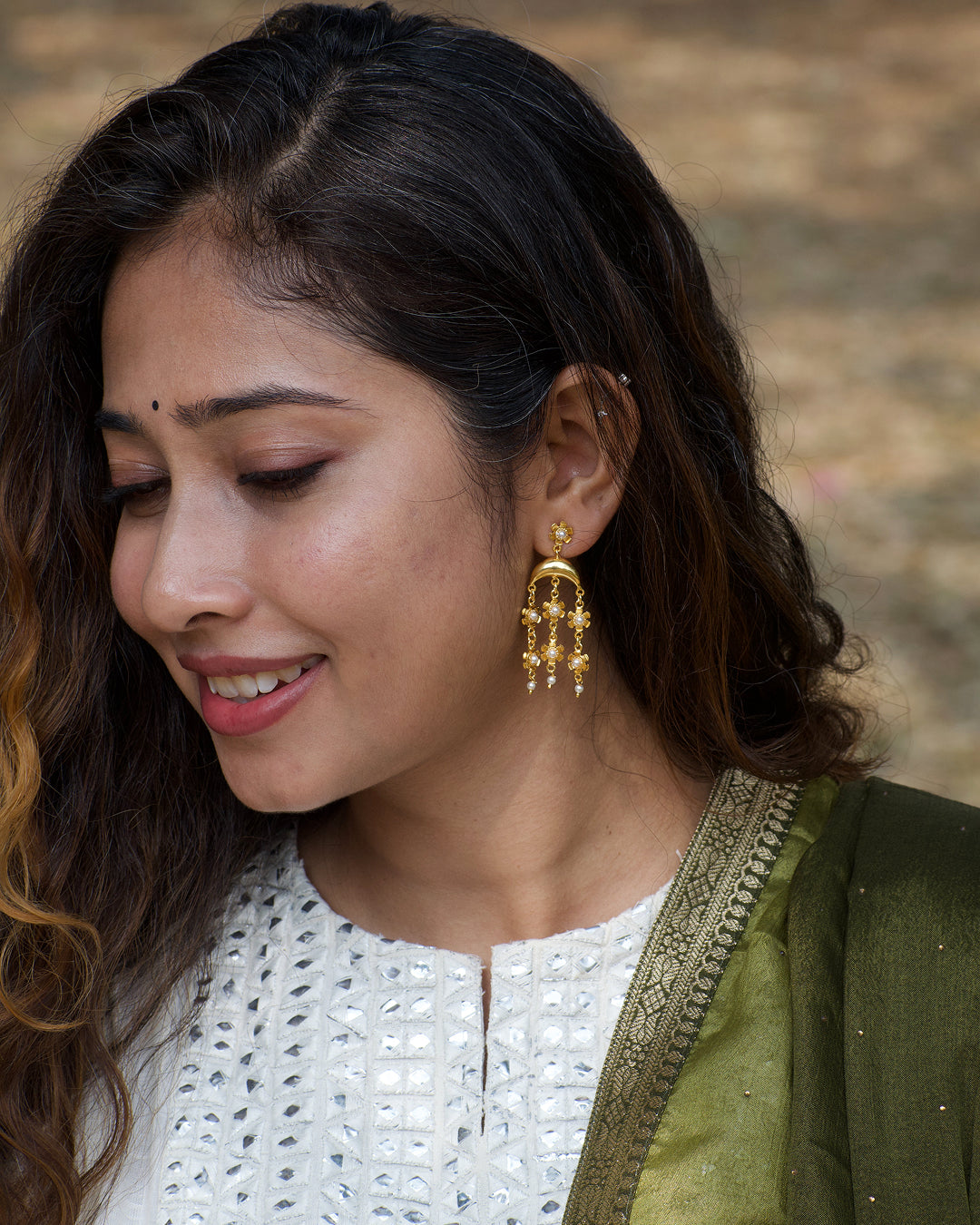 Woman wearing gold earrings with a blurred natural background