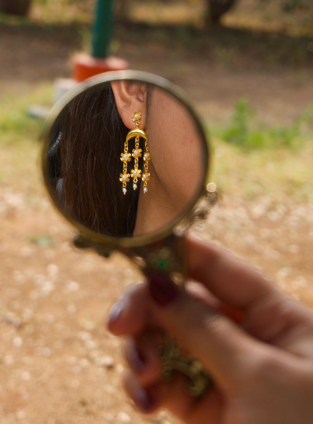 Gold earring visible on a vitage hand mirror.