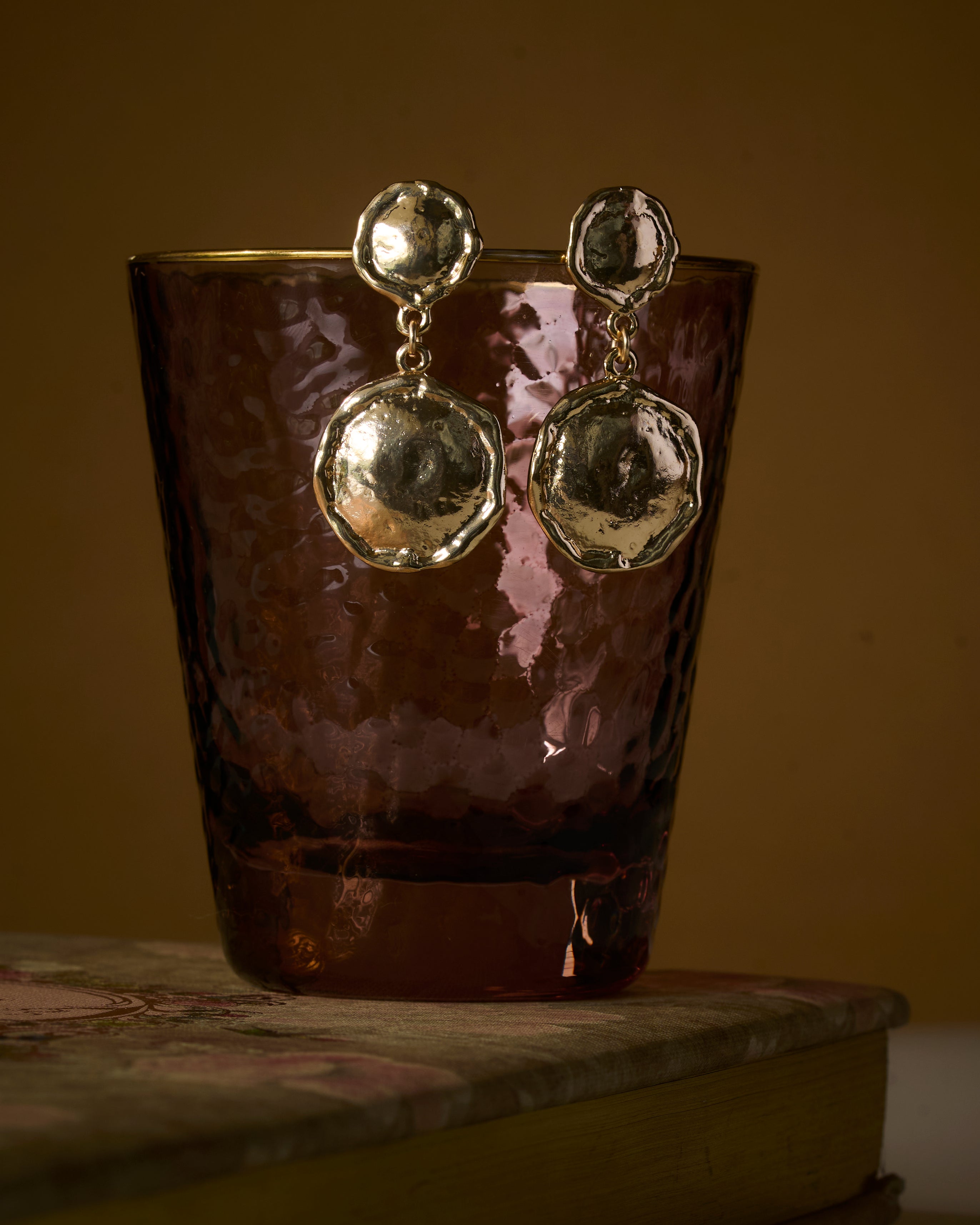 Gold plated earrings with a textured organic finish, on a reflective surface.