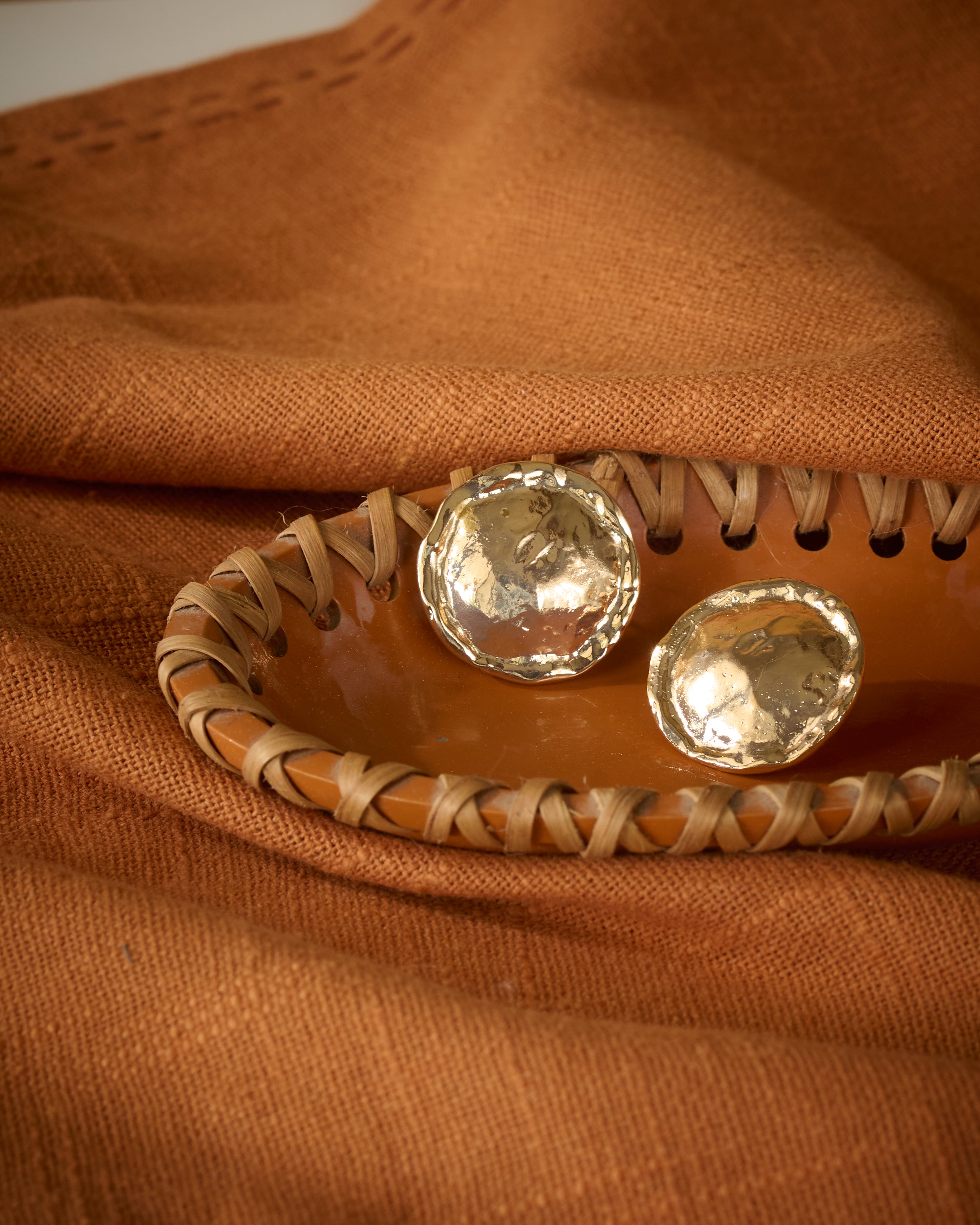 Chunky gold plated textured round stud earrings kept on a terracotta tray.