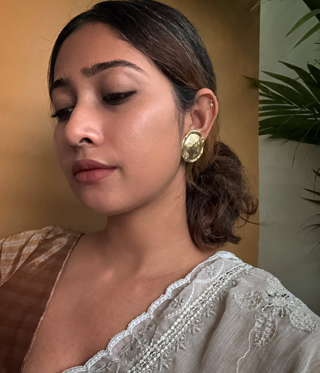 Woman in saree, looking down, wearing gold plated circular textured earrings with a neutral background