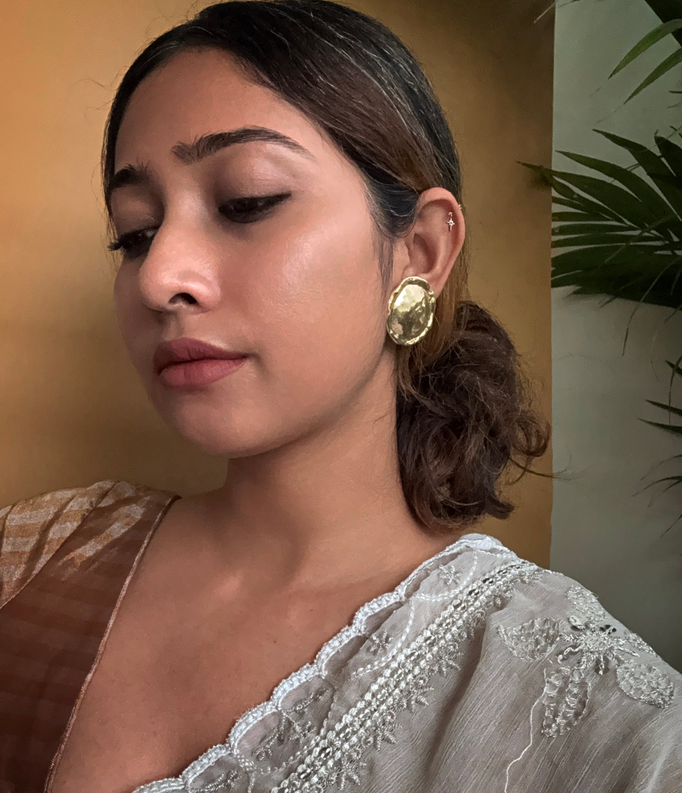 Woman in saree, looking down, wearing gold plated circular textured earrings with a neutral background