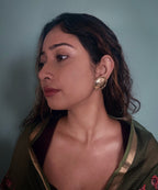 Woman with open messy hair, wearing gold plated circular textured earrings with a teal background