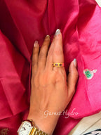 Garnet Hydro ring with three red stones set along a gold band, worn on a hand resting on pink silk