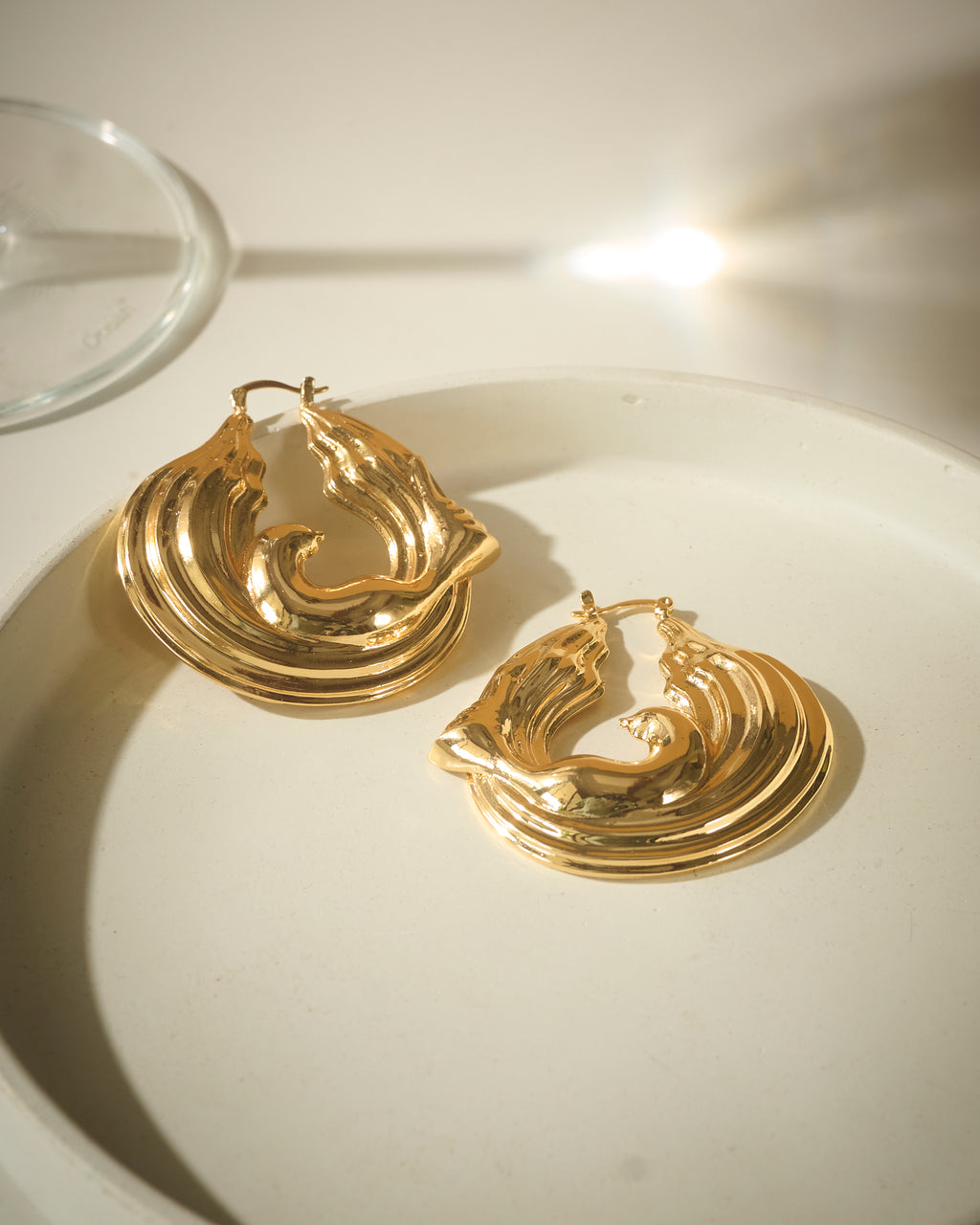 Gold plated chunky hoop earrings with ripple effect on a light surface