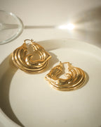 Gold plated chunky hoop earrings with ripple effect on a light surface