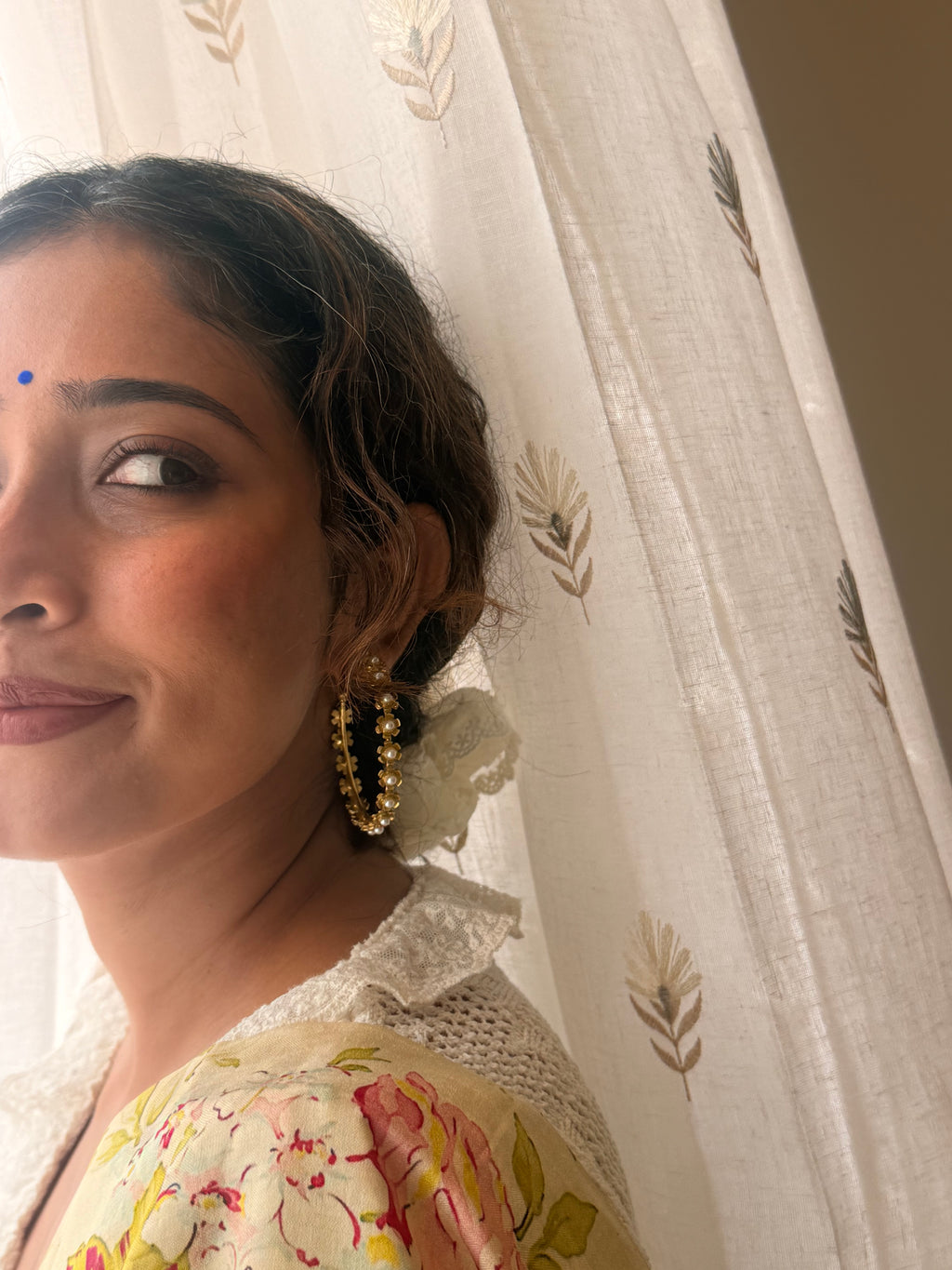 Close-up of a woman wearing Gulnaar Hoops, gold flower and pearl detailing visible near the ear, soft bindi, floral saree with crochet blouse, warm natural light.