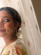 Close-up of a woman wearing Gulnaar Hoops, gold flower and pearl detailing visible near the ear, soft bindi, floral saree with crochet blouse, warm natural light.