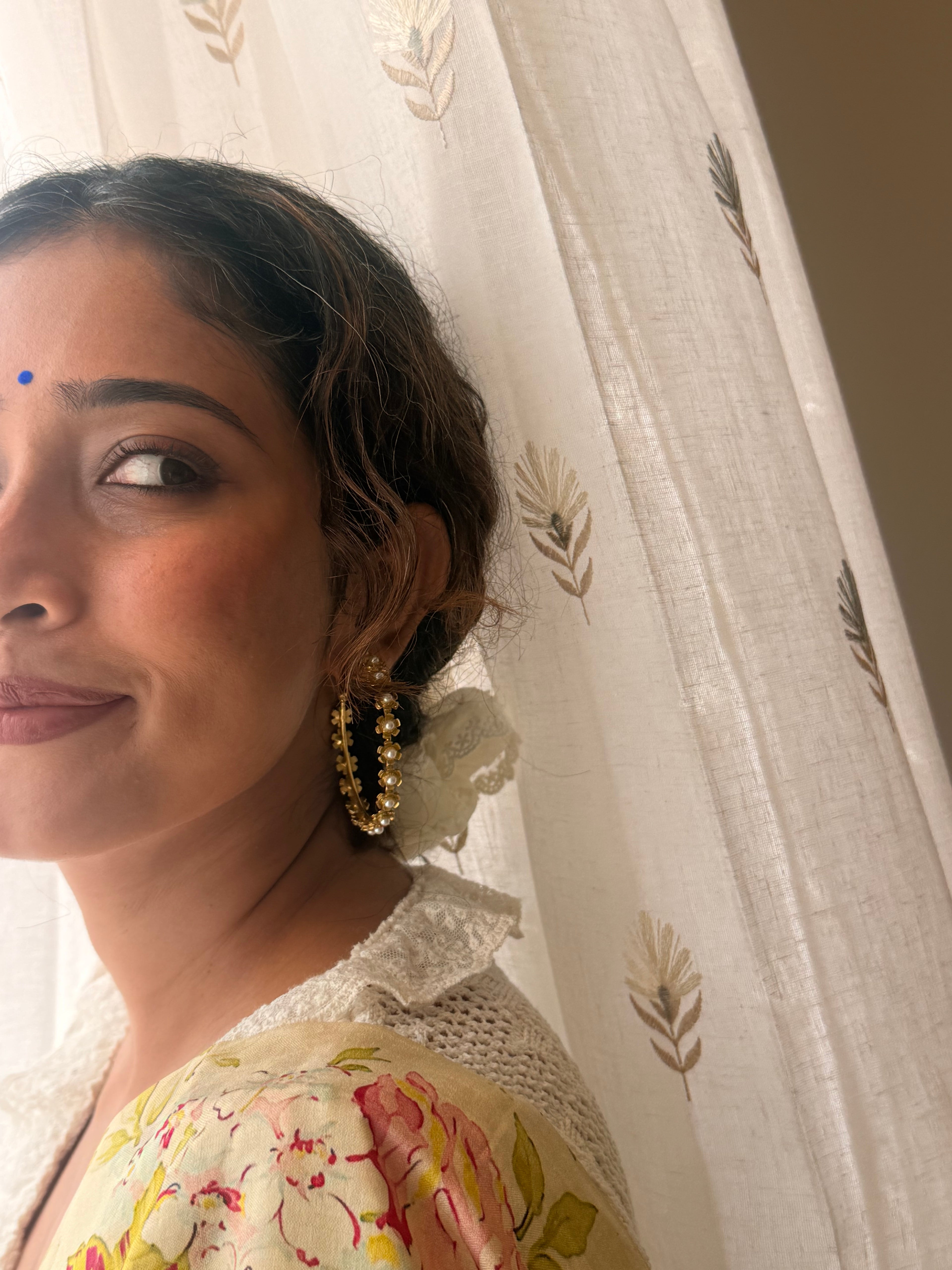 Close-up of a woman wearing Gulnaar Hoops, gold flower and pearl detailing visible near the ear, soft bindi, floral saree with crochet blouse, warm natural light.