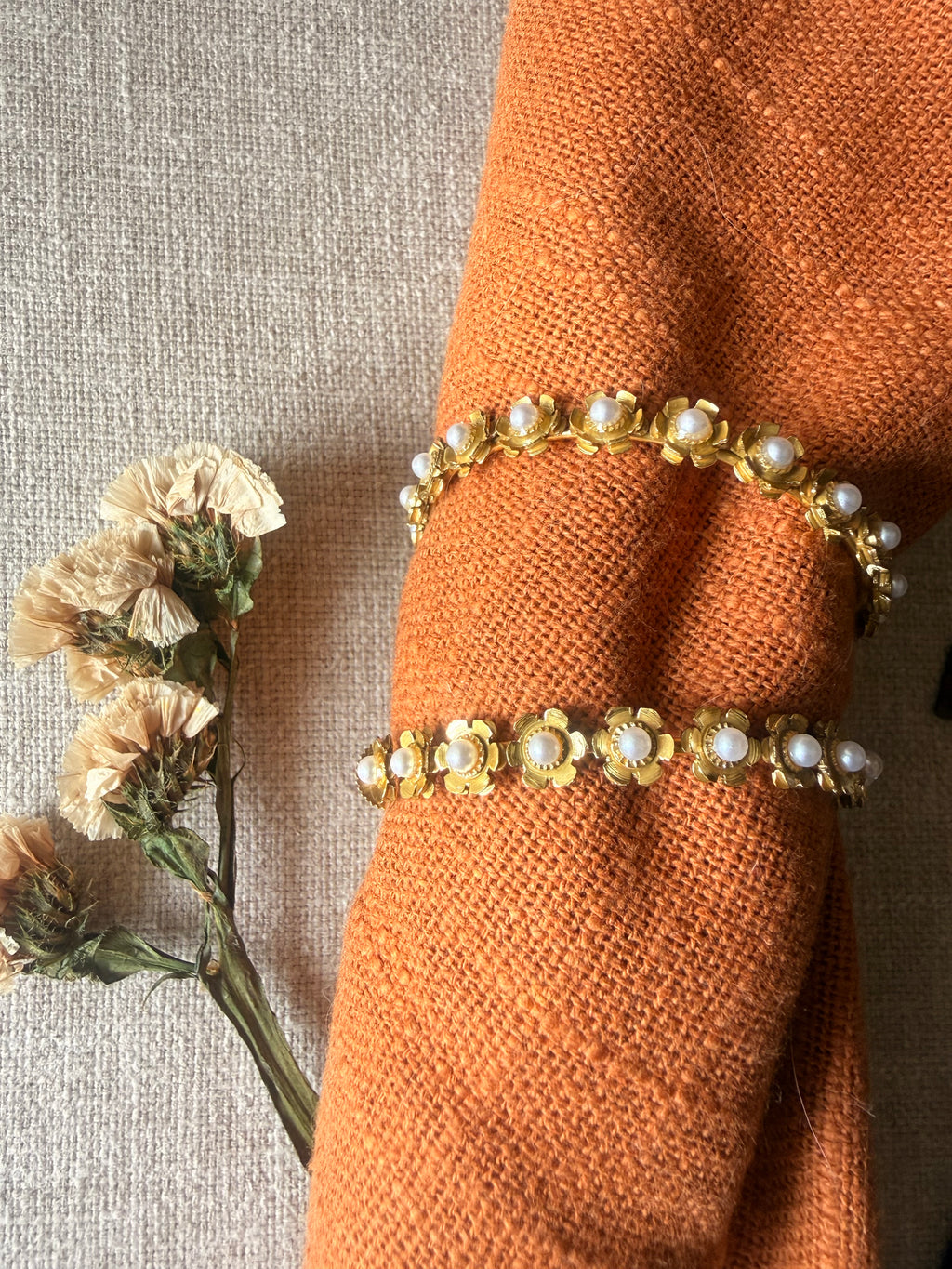 Close up of gulnaar hoops displayed on an orange fabric napkin over a gray textured surface with dried flowers.