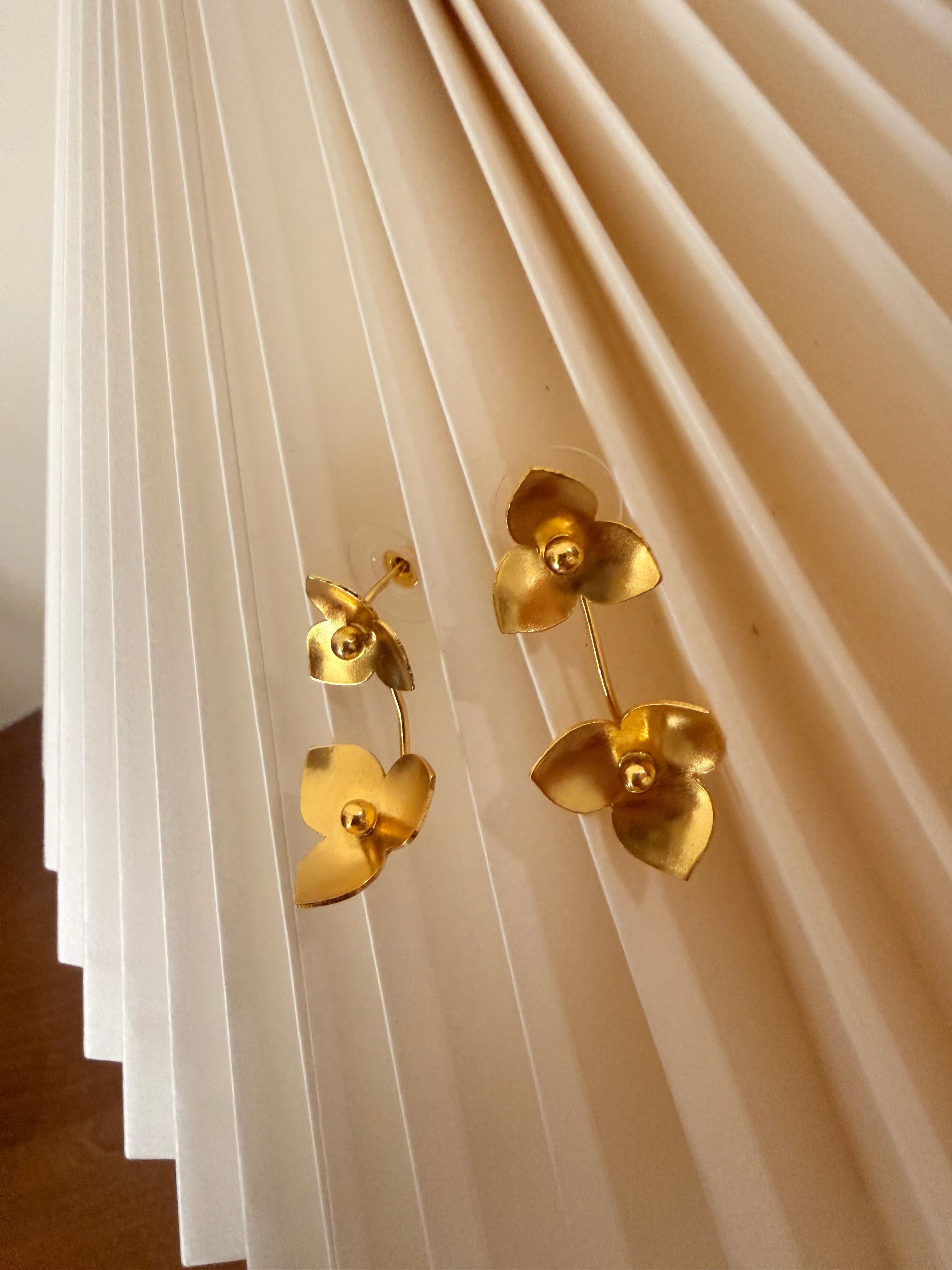 Gold plated double flower-shaped earrings on a textured beige surface