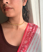 Gold plated brass Motiya Choker with jasmine-shaped flowers worn close to the collarbone, styled with a brown fitted top and a red floral saree dupatta in soft natural window light.