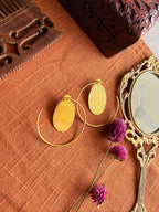 Gold-plated brass hoop earrings with oval textured disc on terracotta fabric, styled with a vintage mirror and dried purple Globe Amaranth flowers