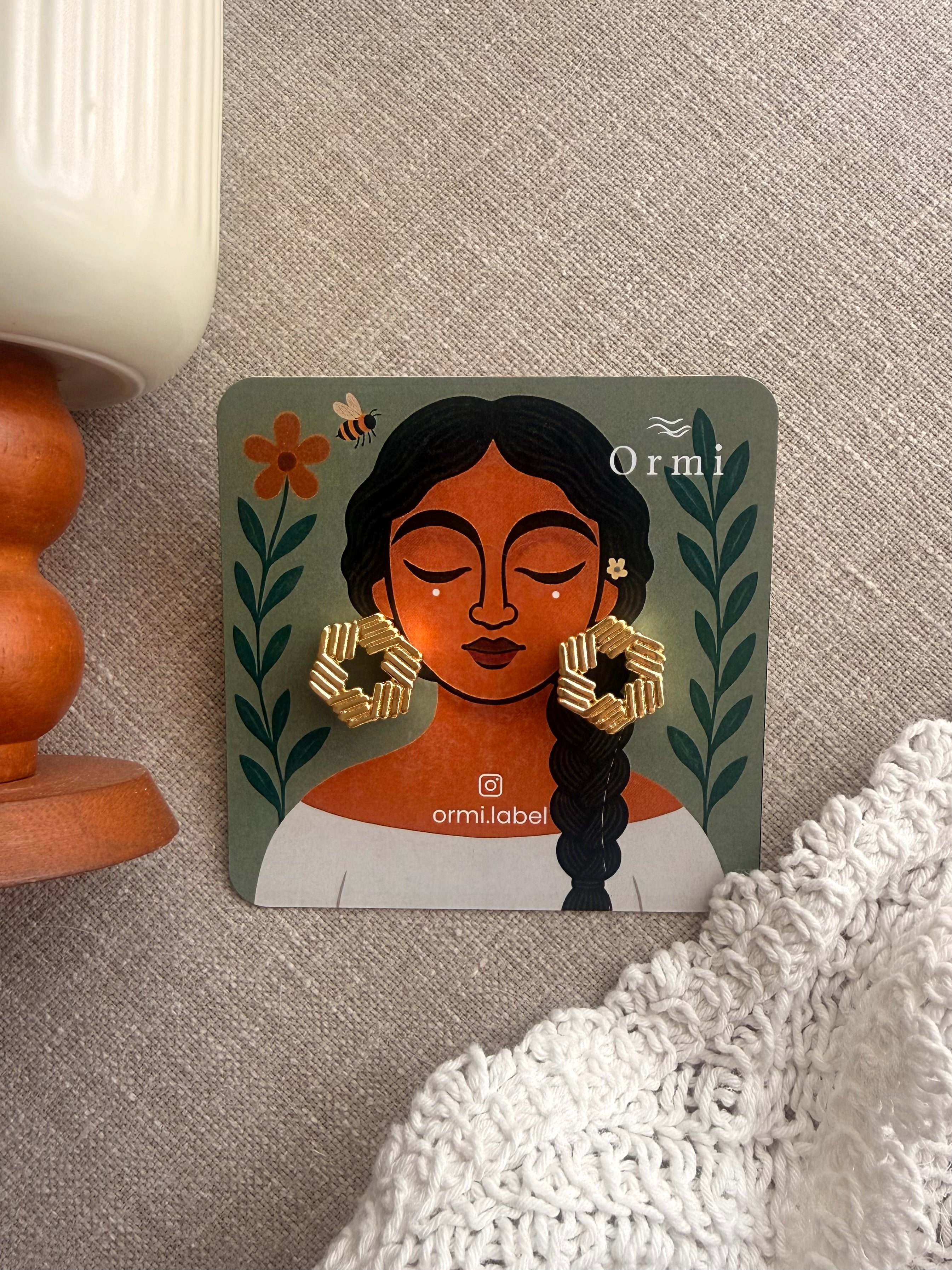 Ormi branded earring card displaying Yantra studs, illustrated packaging with pretty woman and botanical motifs in terracotta and green