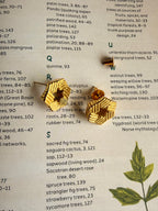 Yantra studs placed on open book index page alongside dried botanical illustration, close-up showing hexagonal structure and textured ridged edges