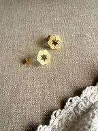 Yantra studs flatlay on grey linen fabric with white lace, showing the hollow hexagon shape and ridged edges, soft natural light
